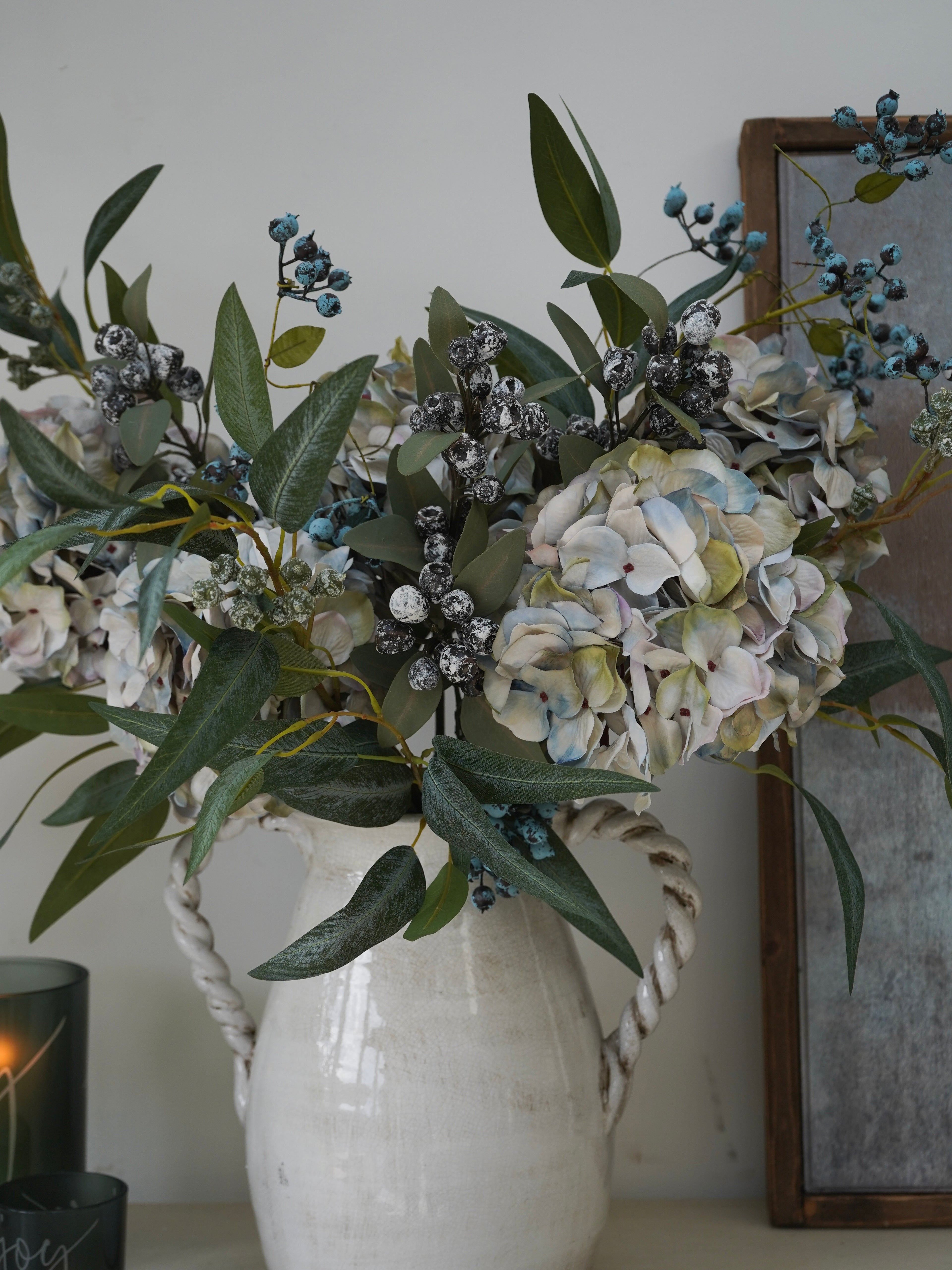 Christmas floral arrangement in a white vase with greenery and hydrangeas on a neutral background