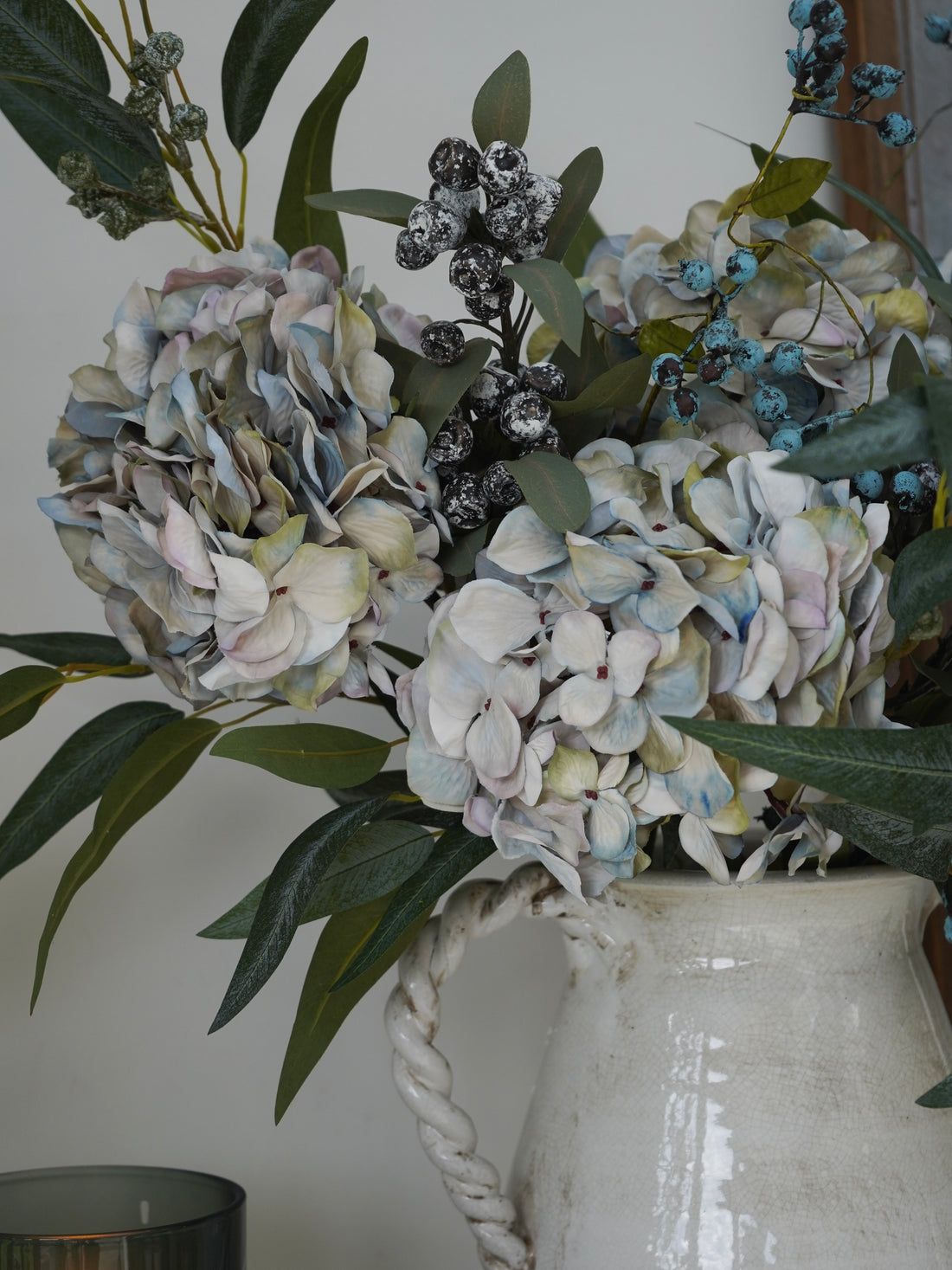 Floral arrangement with hydrangeas and berries in a white vase against a neutral background