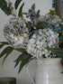 Floral arrangement with hydrangeas and berries in a white vase against a neutral background