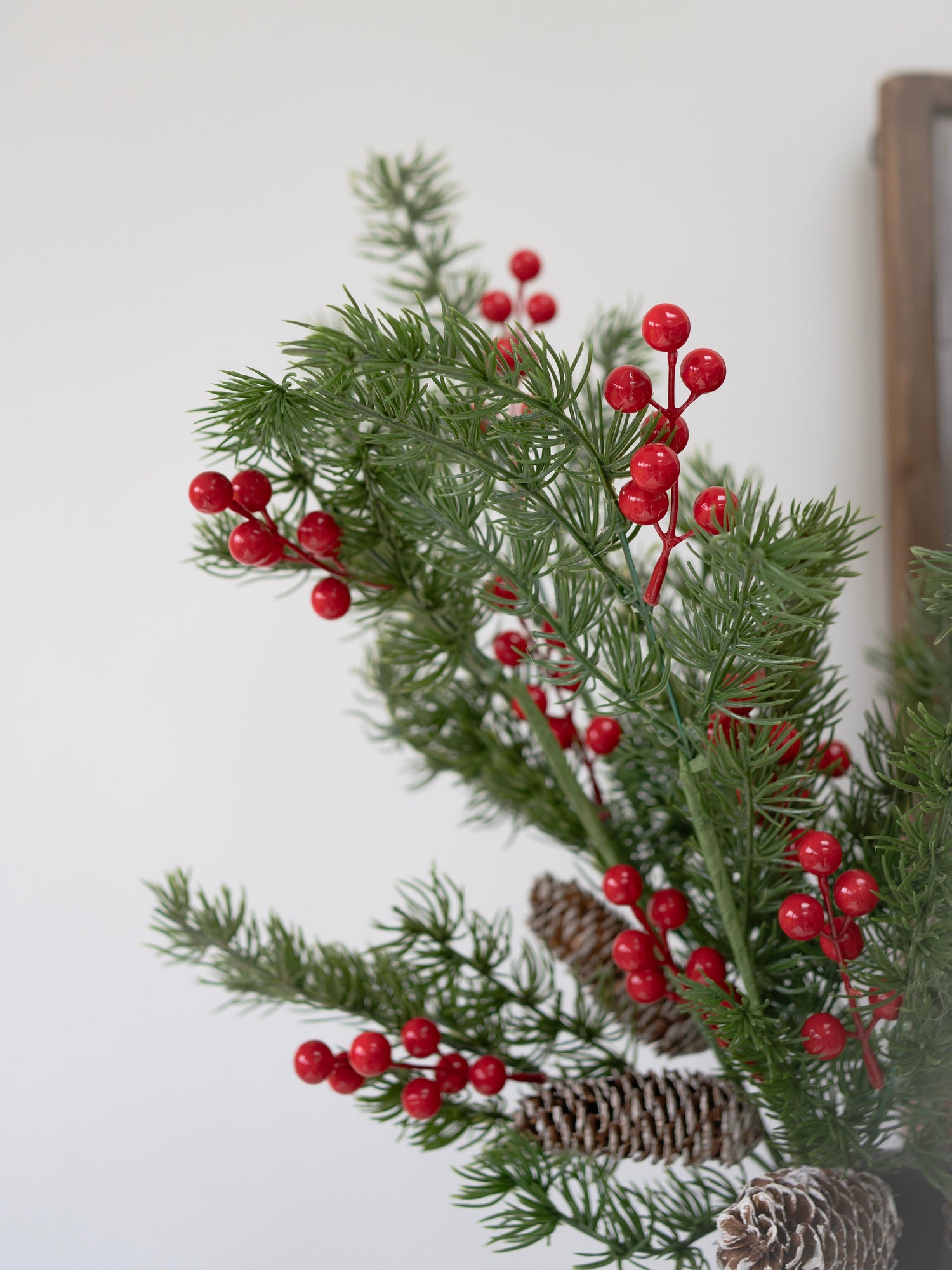 Decorative faux christmas foliage arrangement with red berries and pine cones on a white background