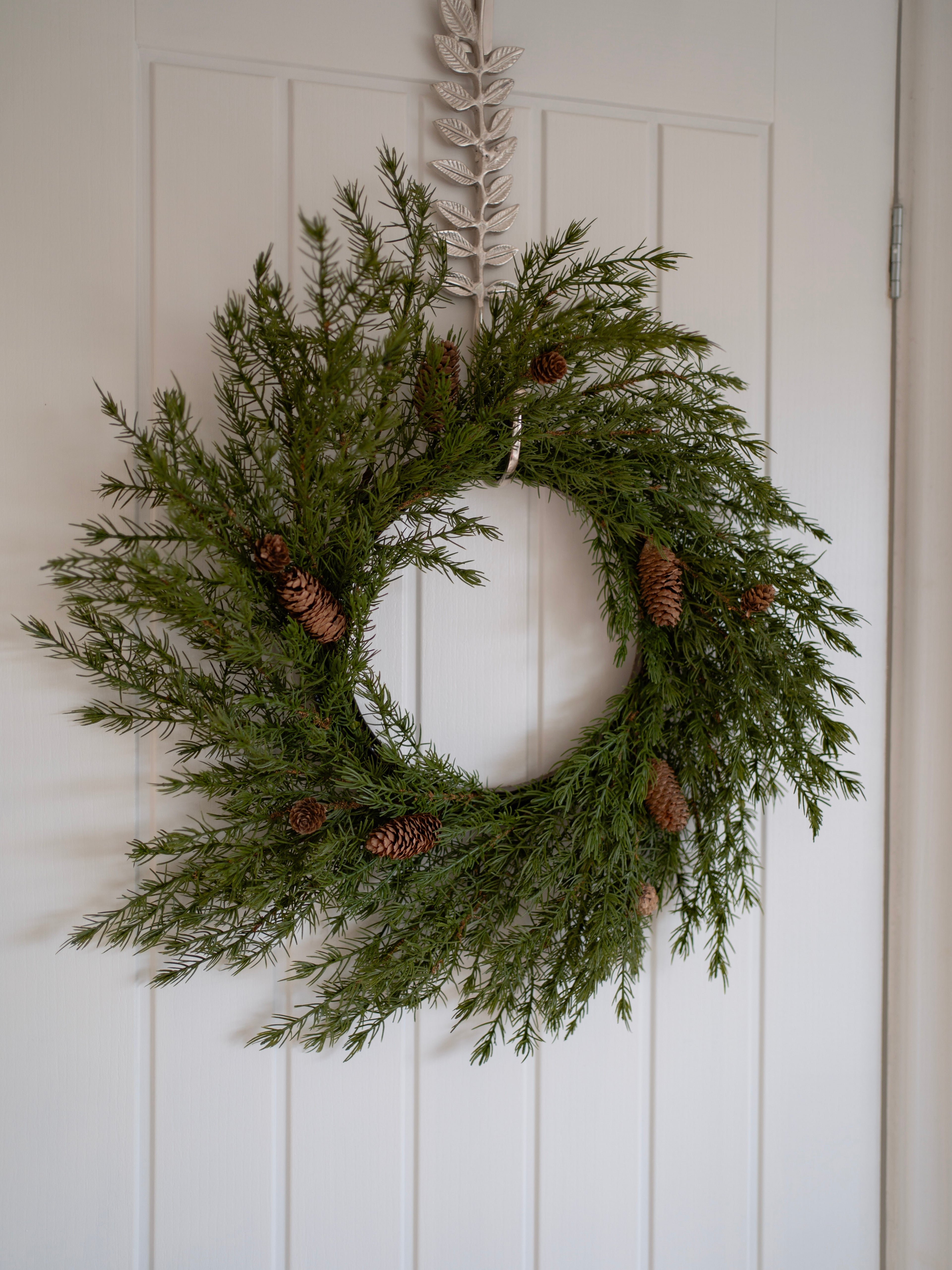 faux christmas foliage wreath with pinecones on a white door