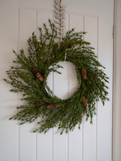 faux christmas foliage wreath with pinecones on a white door
