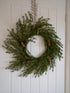 faux christmas foliage wreath with pinecones on a white door