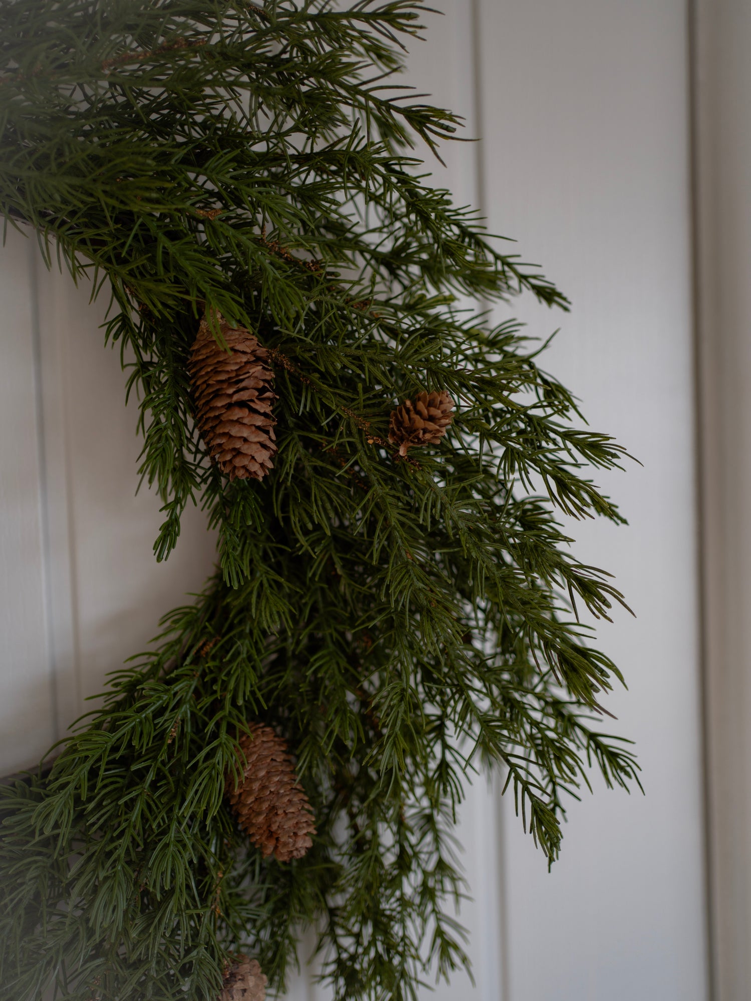 faux woodland wreath with pine cones on a white paneled wall