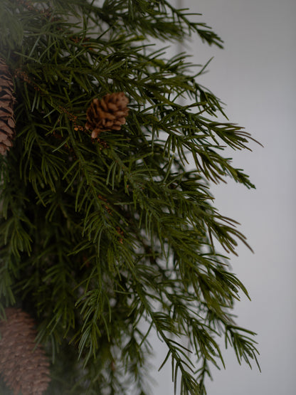 Close-up of faux green pine wreath with pinecones on a white background