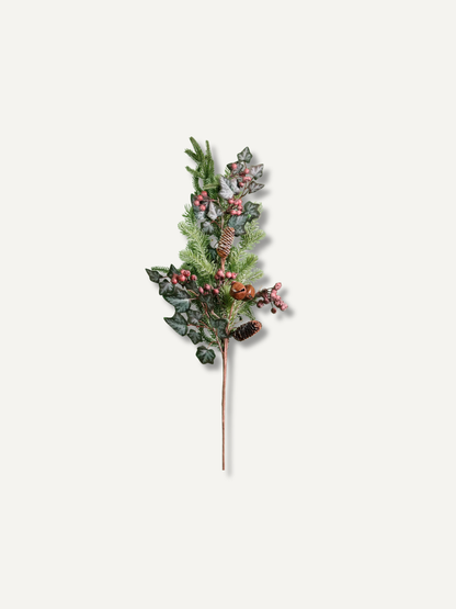 A single artificial winter branch with green pine needles, dark holly leaves, and small red berries on a thin brown stem, centered on a plain light warm-gray background.