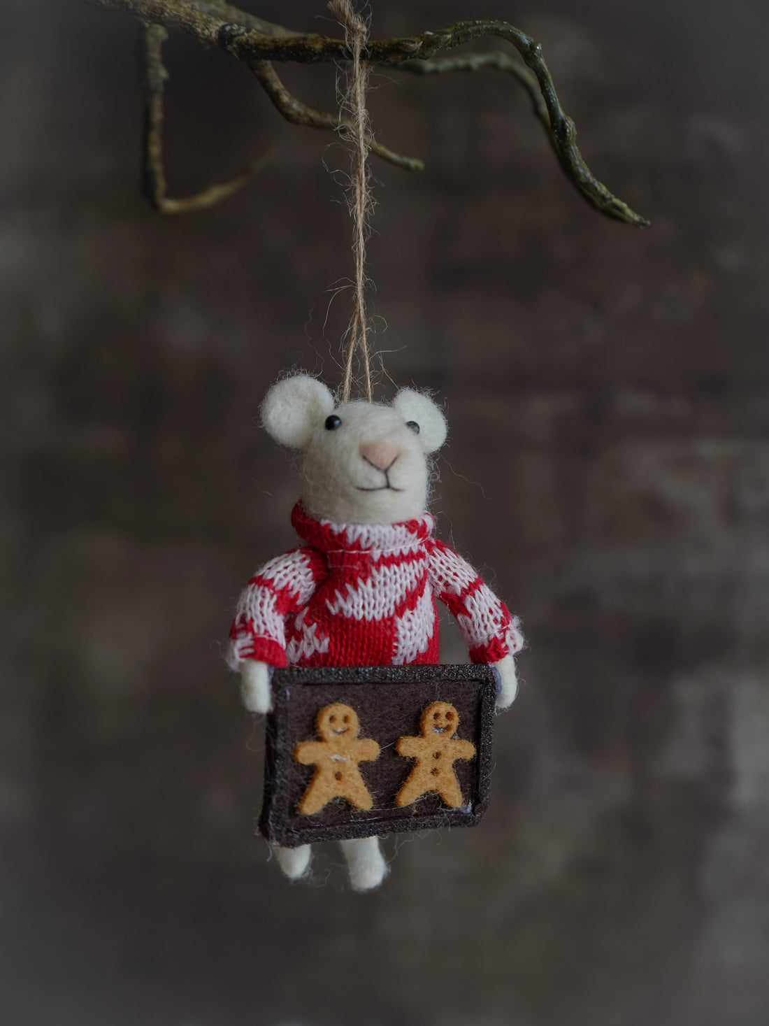 Small knitted mouse ornament wearing a red sweater with a box of gingerbread men on a dark background.