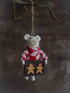 Small knitted mouse ornament wearing a red sweater with a box of gingerbread men on a dark background.
