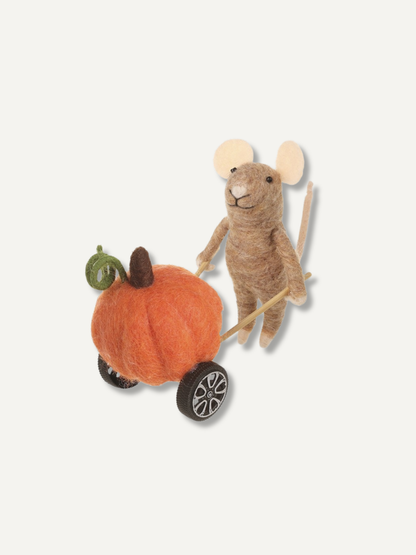 A felted wool toy mouse pushing a small orange pumpkin cart with black wheels, photographed on a plain light background.