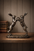 Bronze sculpture of two boxing hares on a wooden surface with a neutral background