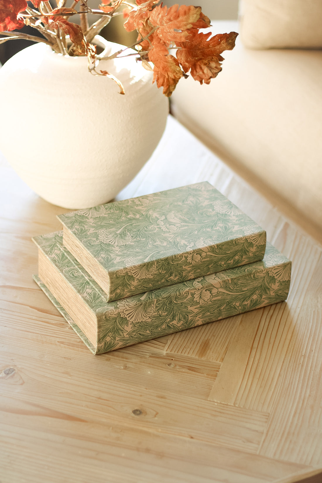 Two decorative boxes with floral patterns on a wooden surface, with a vase and flowers in the background.
