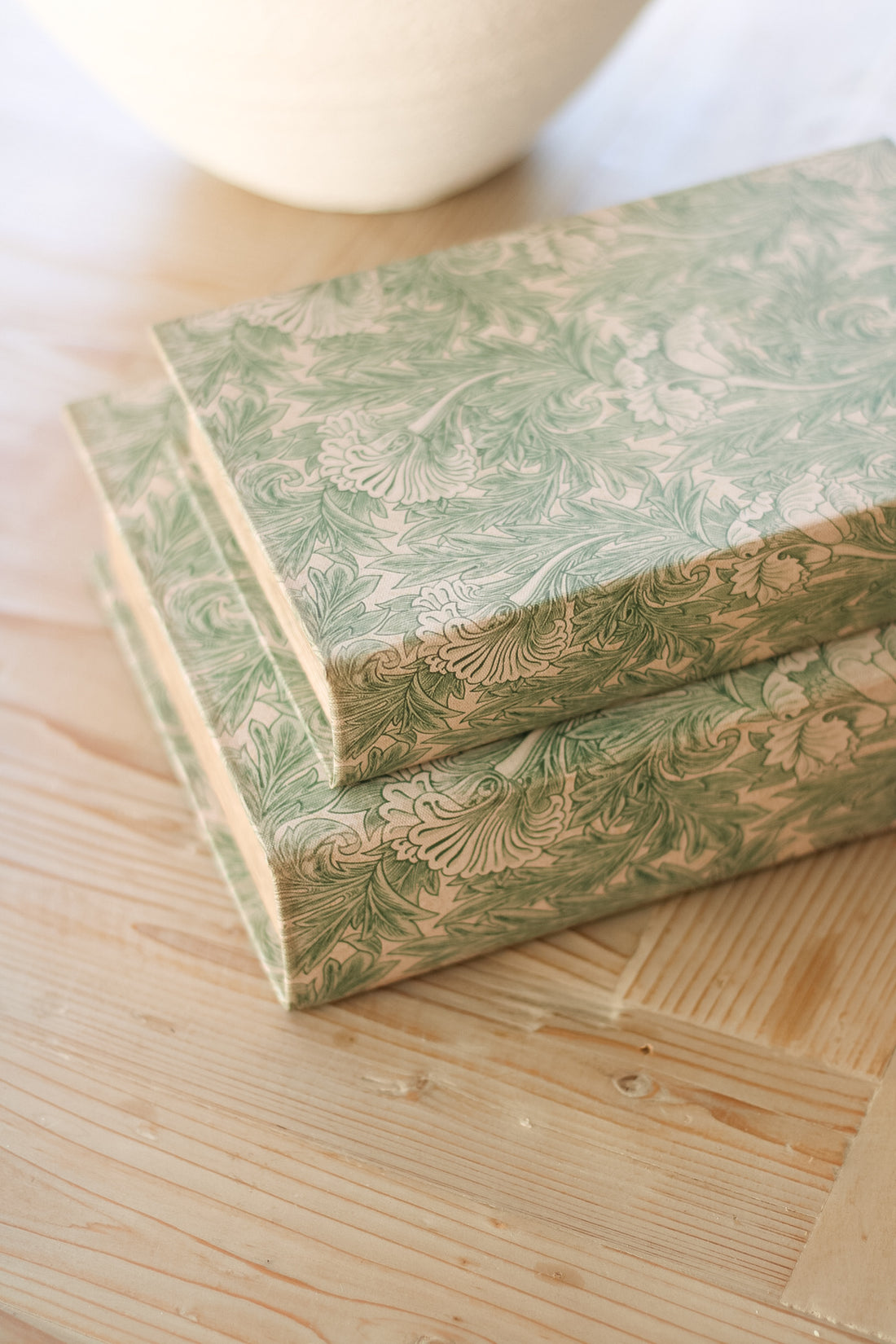 Two green floral books stacked on a wooden surface