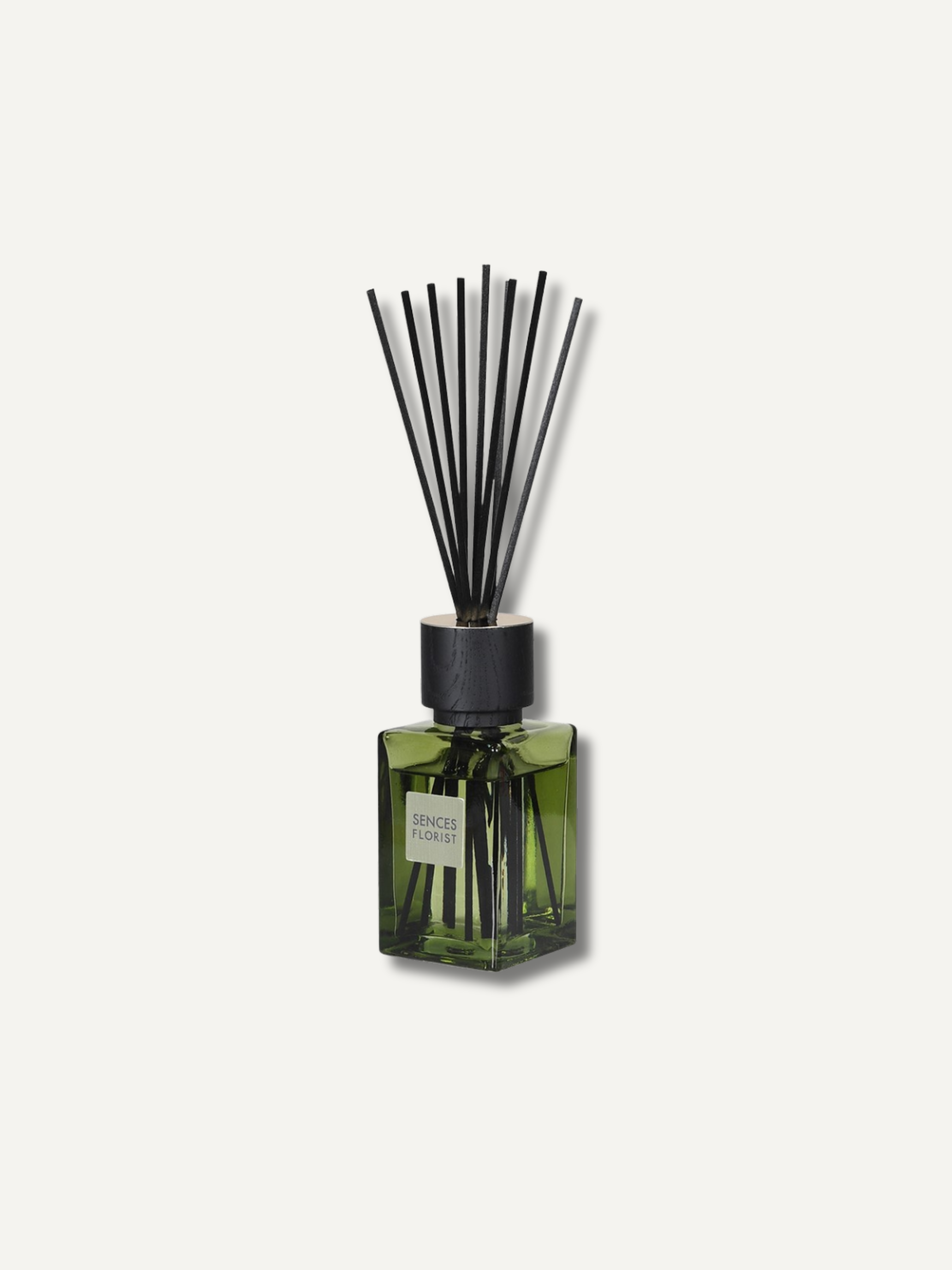A reed diffuser bottle with a translucent olive green glass body, a black cap, and black reeds, shown against a light off-white background.