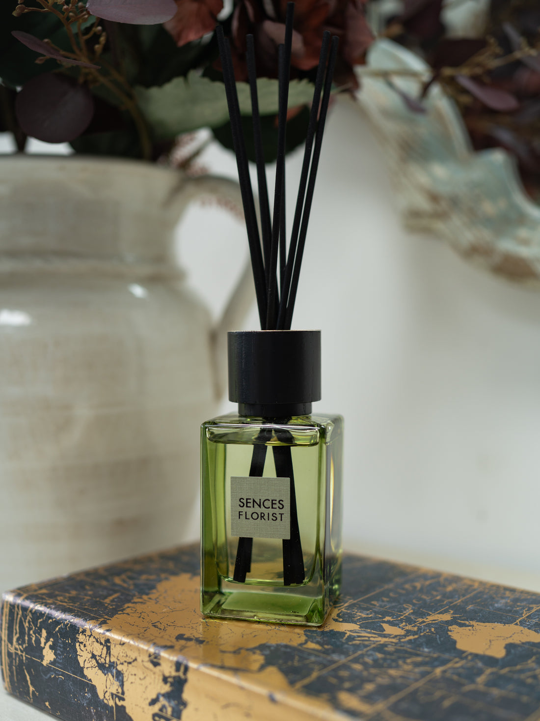 A reed diffuser bottle with pale green liquid and black reeds, labeled &