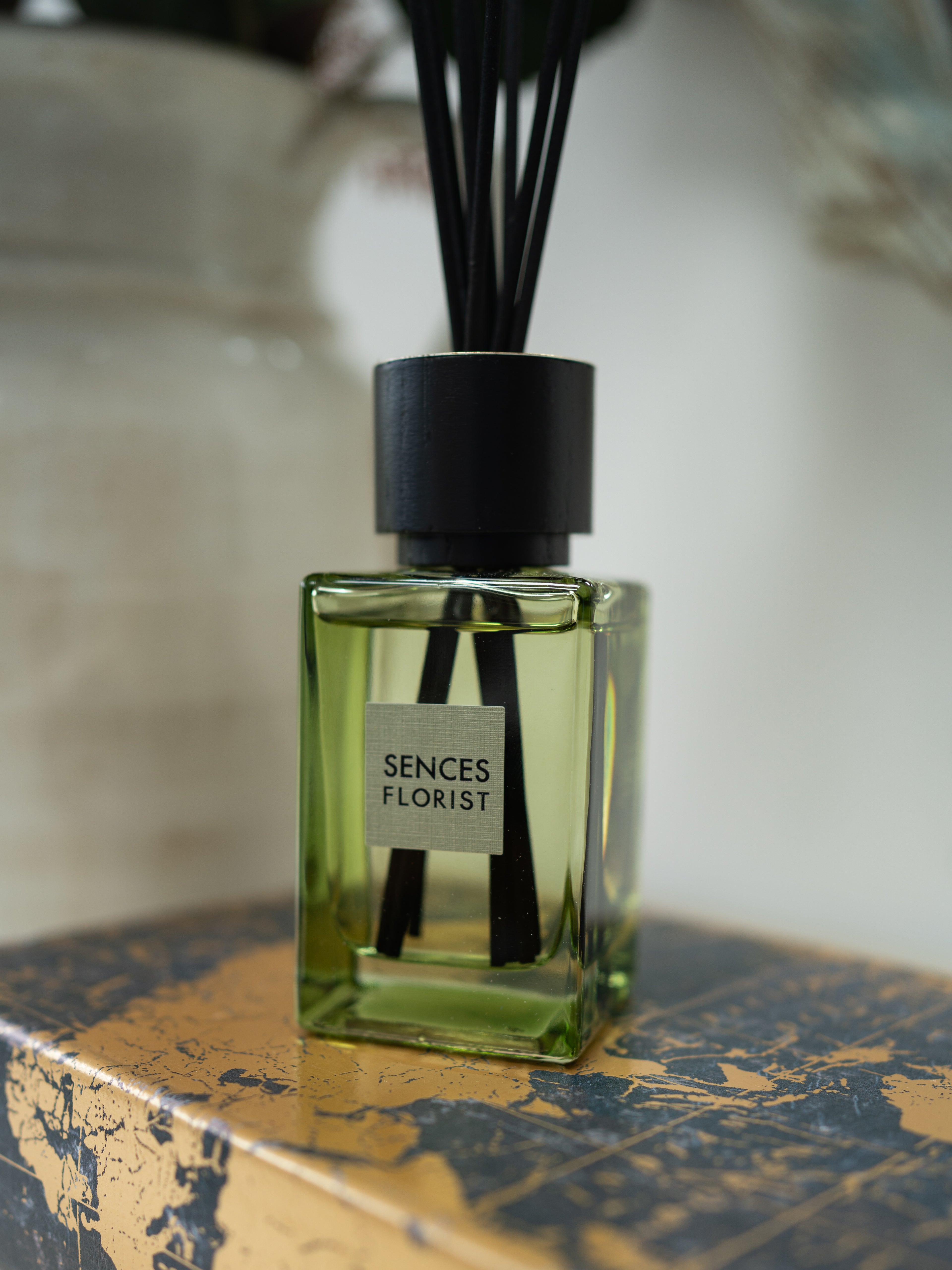 A glass reed diffuser bottle filled with light green liquid, with black reeds and a black cap, labeled &