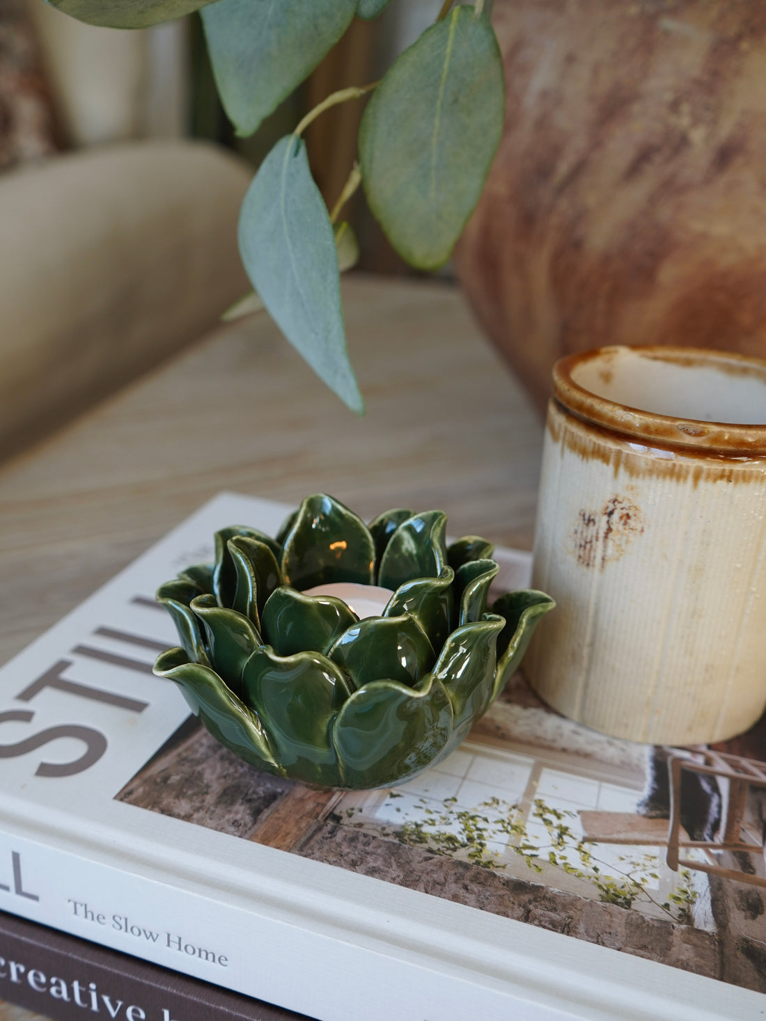 Green ceramic candle holder on a book with a rustic mug in the background