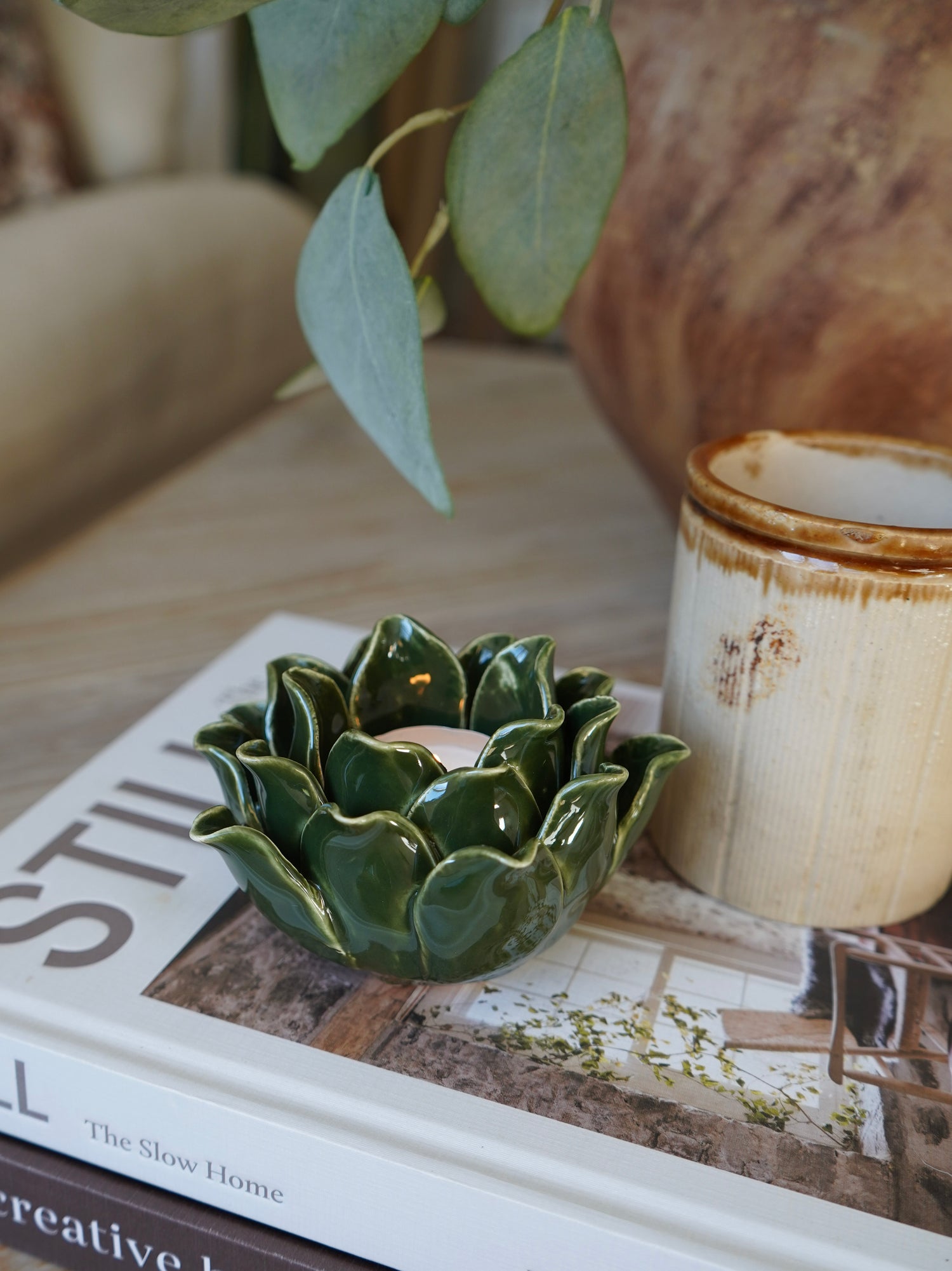 Green ceramic candle holder on a book with a rustic mug in the background