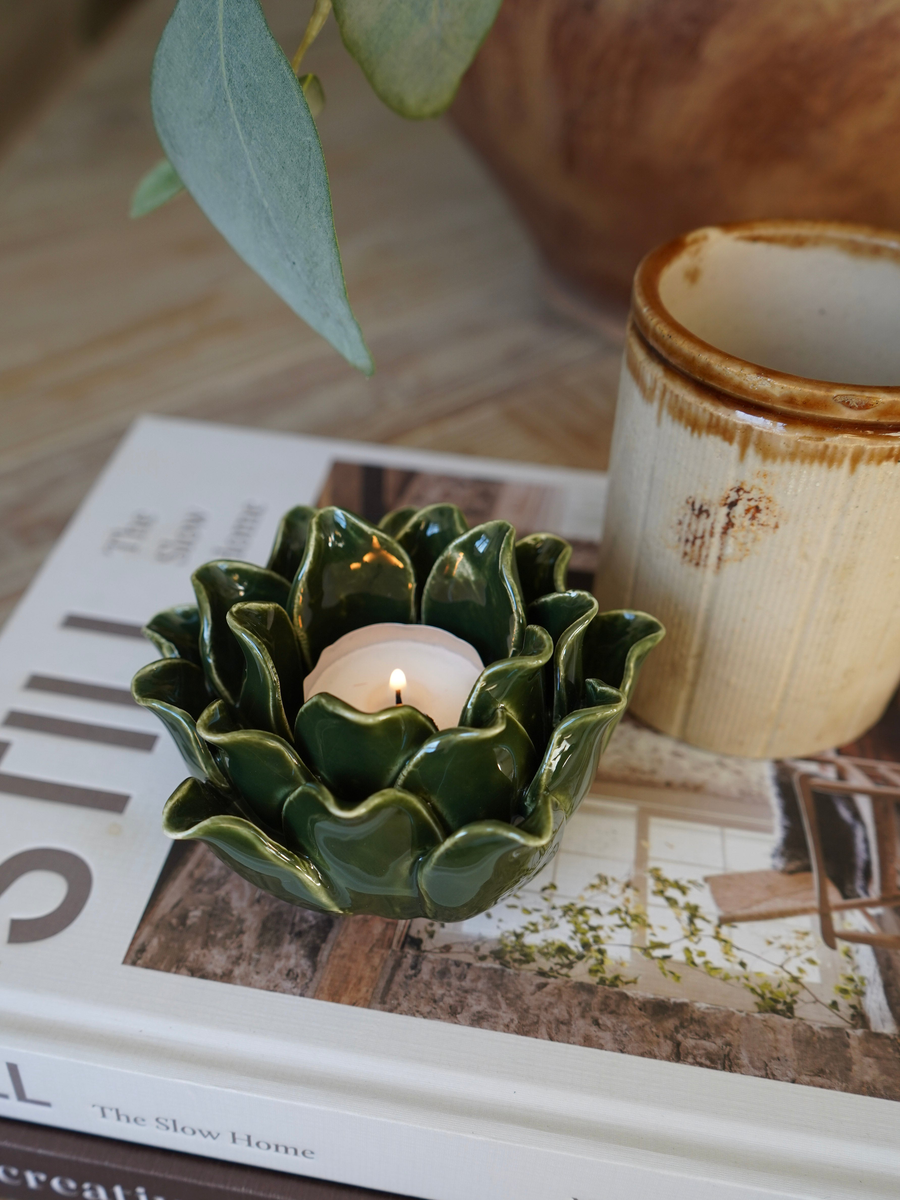 Green ceramic candle holder with a lit candle on a magazine