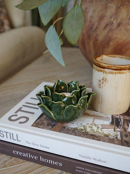 Green ceramic artichoke-shaped candle holder on a book with a blurred background