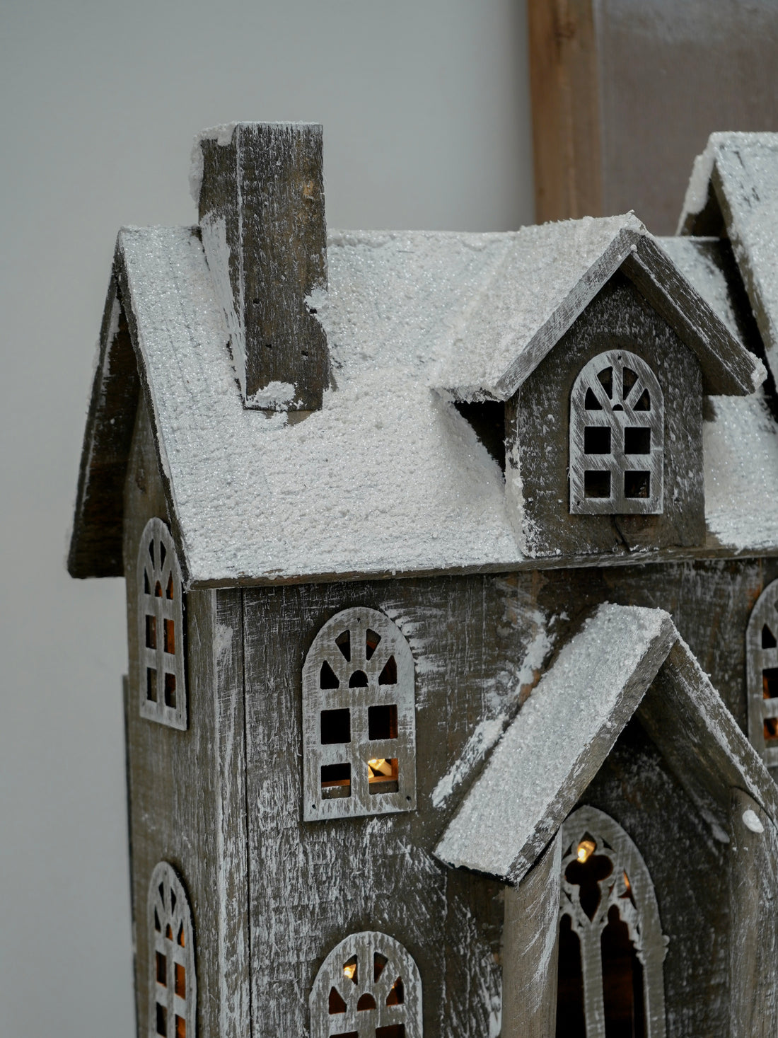 Wooden model of a house with snow on the roof against a plain background