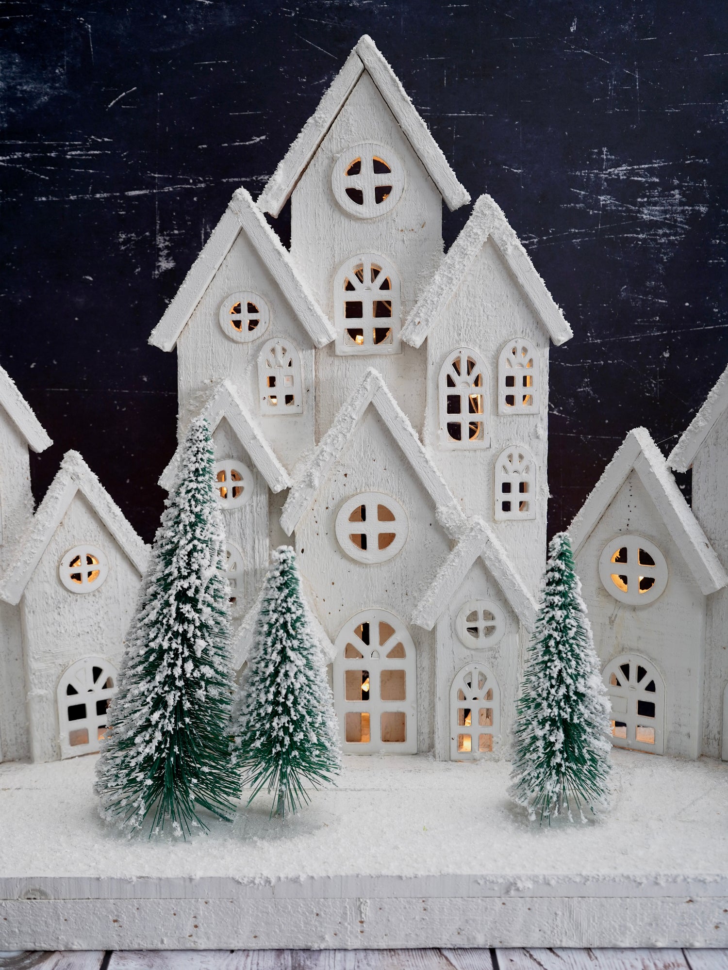 Decorative white house with lit windows and snow-covered trees against a dark background