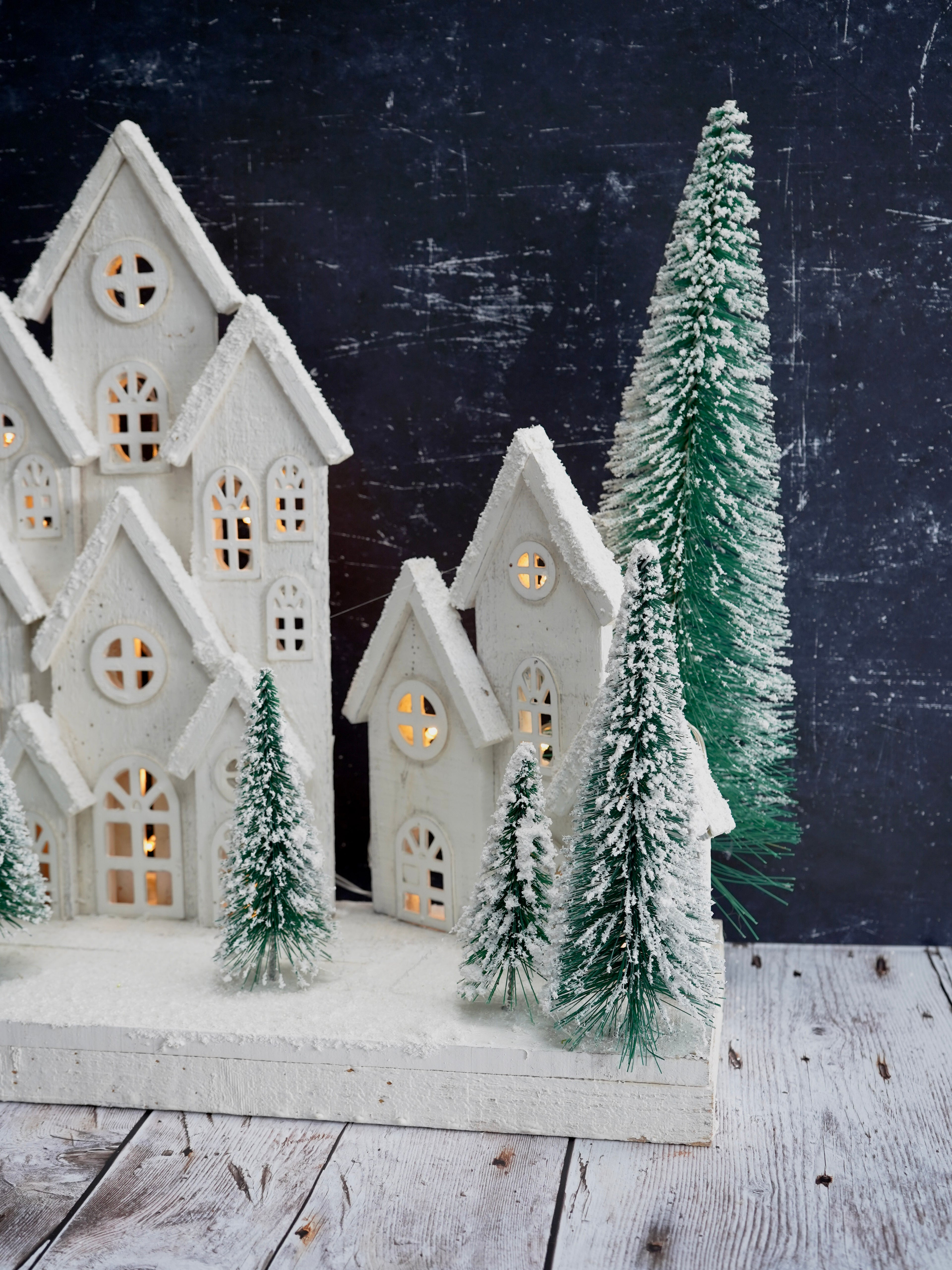 Decorative winter scene with white houses and snow-covered trees on a dark background