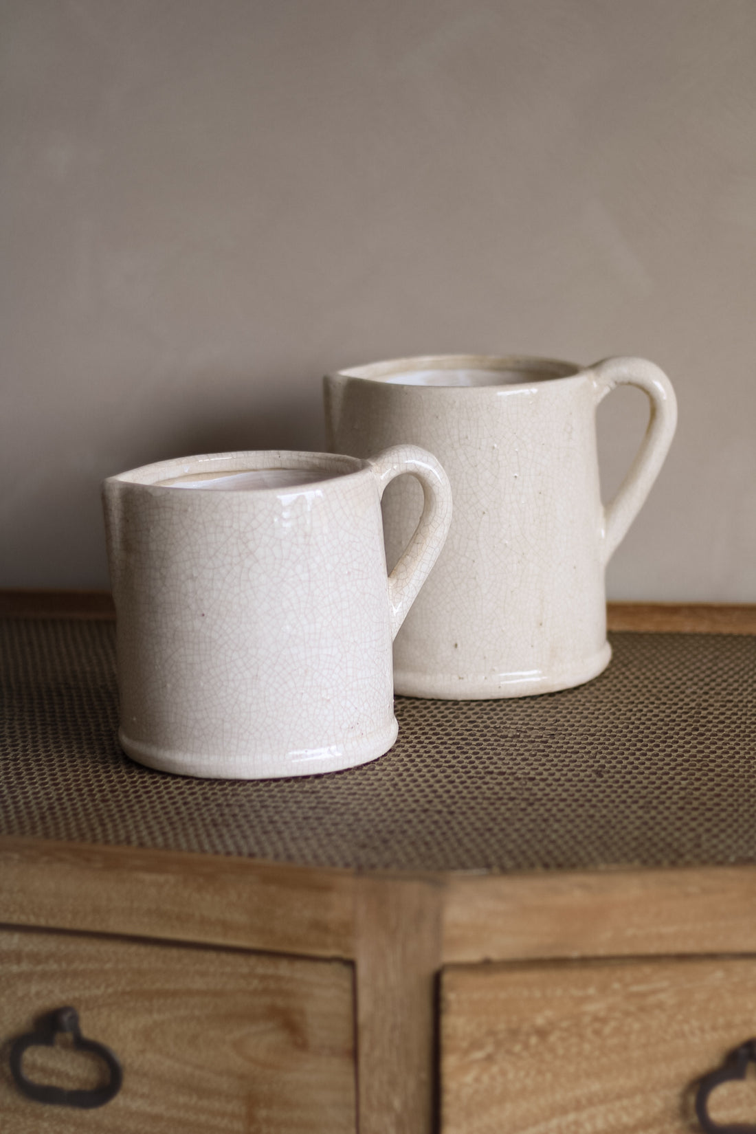 Two ceramic jugs on a textured surface with a neutral background