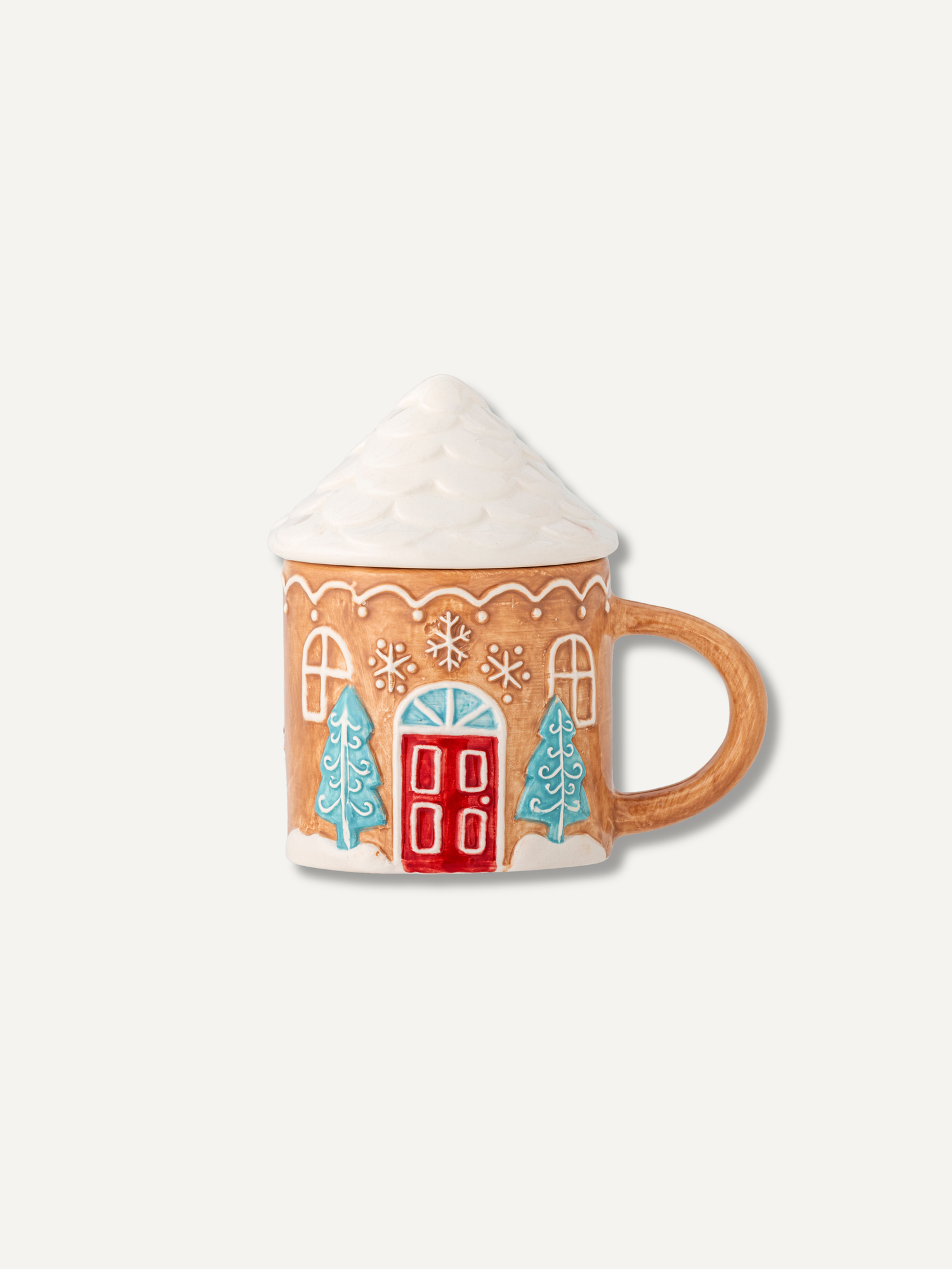 A ceramic mug shaped like a gingerbread house with a snowy roof, decorated with a red door, blue Christmas trees, and white snow details, set against a solid off-white background.