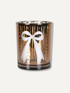 A gold-toned glass candle holder with a white bow design on the front, set against a plain off-white background.