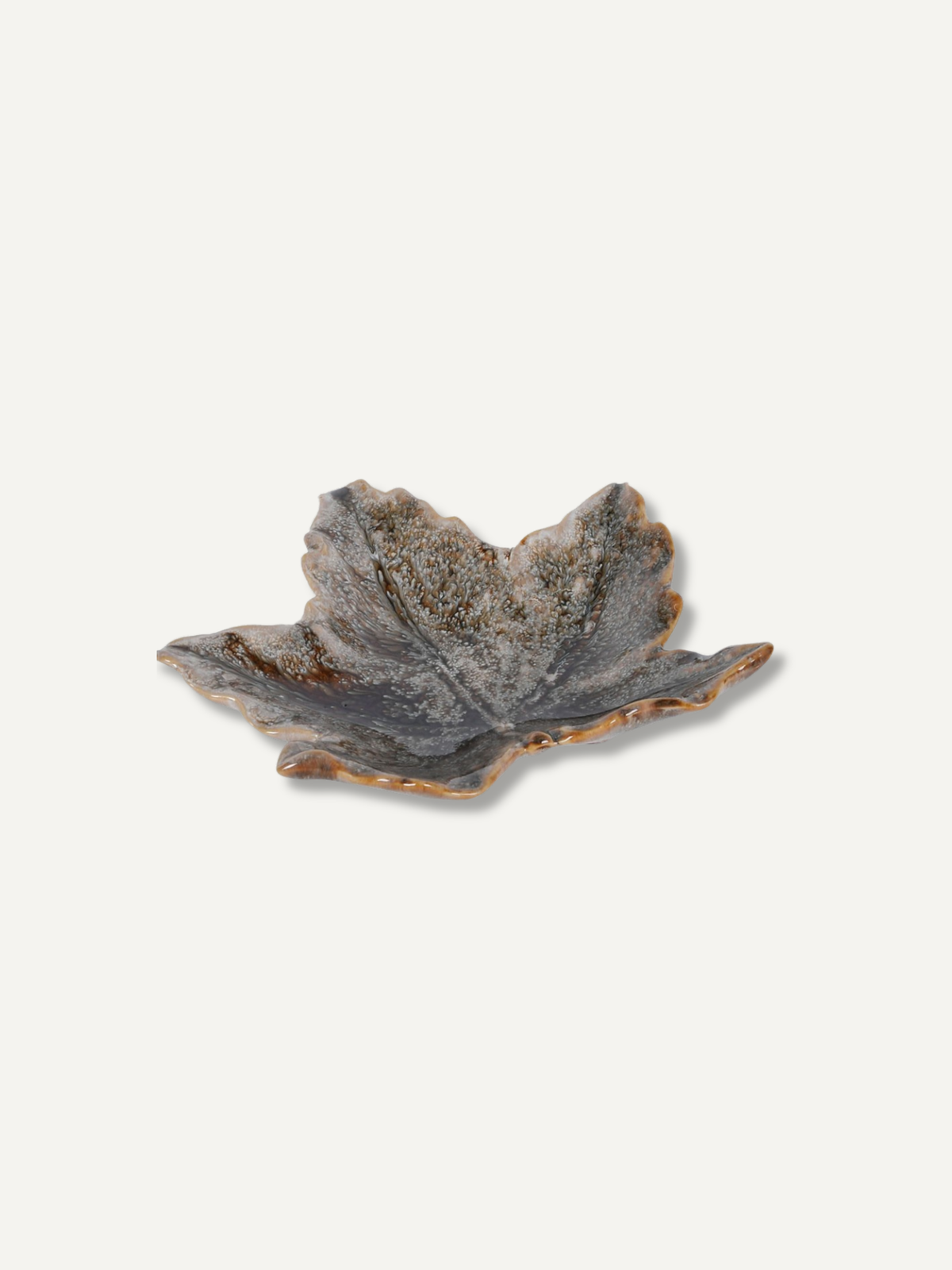 A small leaf-shaped ceramic dish with a textured, speckled glaze in earthy gray, brown, and beige tones, set against a solid off-white background.