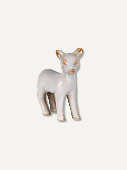 A small ceramic deer figurine in a glossy off-white glaze with subtle gold accents on its ears, eyes, and nose, standing against a solid off-white background.