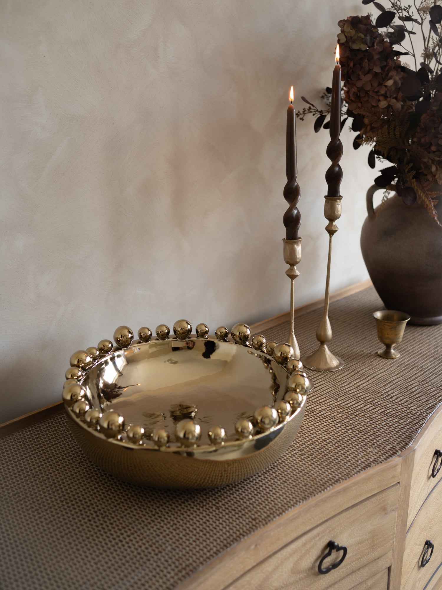 Decorative bowl with spherical design on a textured surface with candles and a vase.