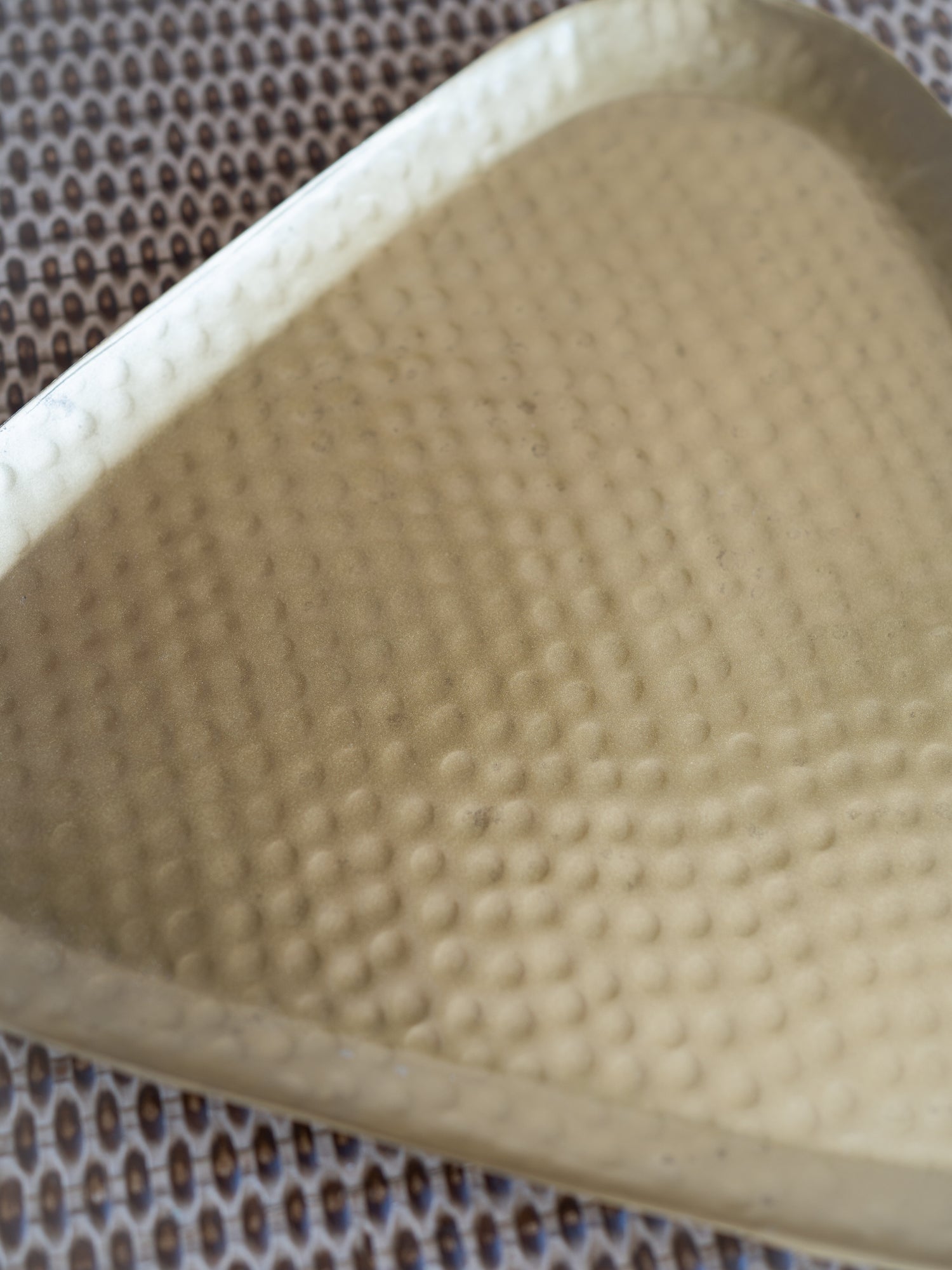 A close-up of a triangular textured tray or dish with a hammered surface, shown resting on a patterned brown and white mat.