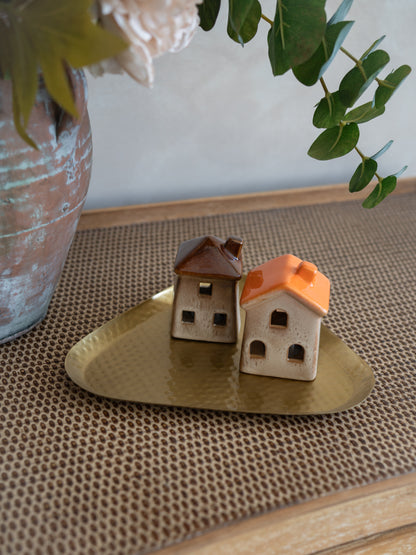 Two miniature ceramic house figurines with one brown roof and one orange roof, displayed on a small gold tray on a woven brown mat.