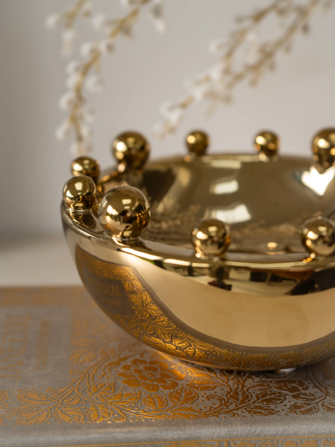 Gold decorative bowl with spherical  bobble accents on a textured surface with floral elements.