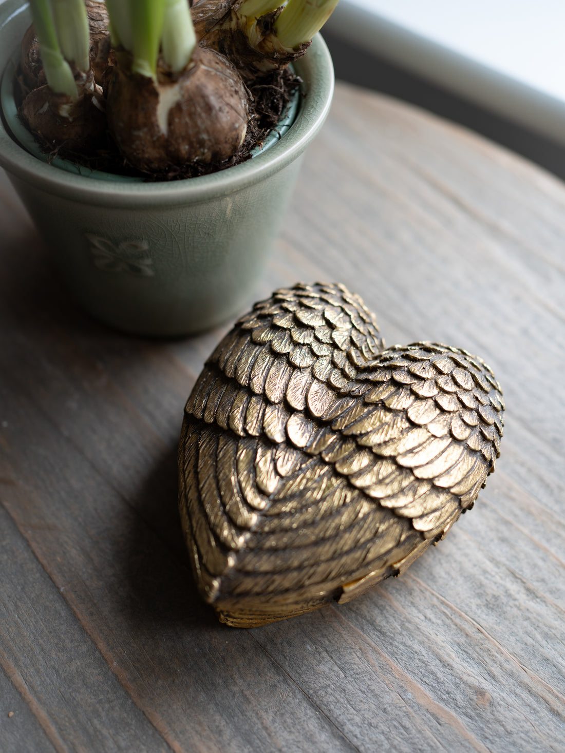 Decorative metallic heart on a wooden surface with a potted plant in the background