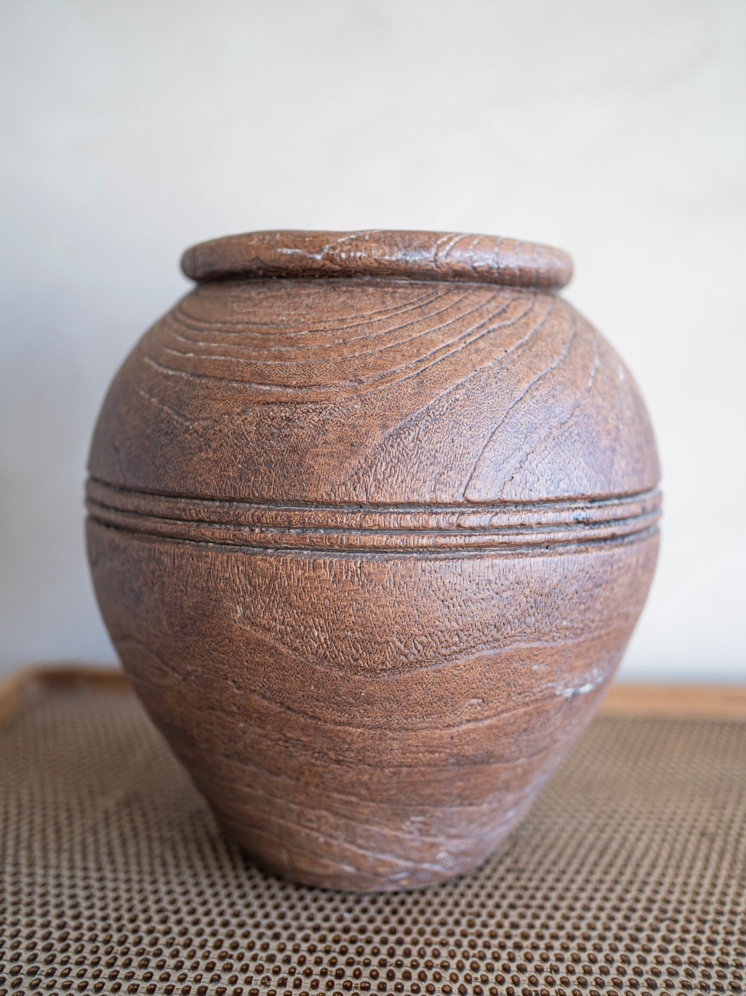 Brown ceramic vase with textured surface on a neutral background