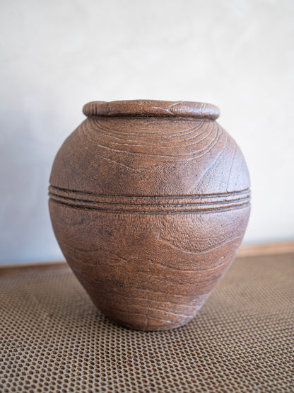 Brown ceramic urn  vase on a textured surface with a neutral background