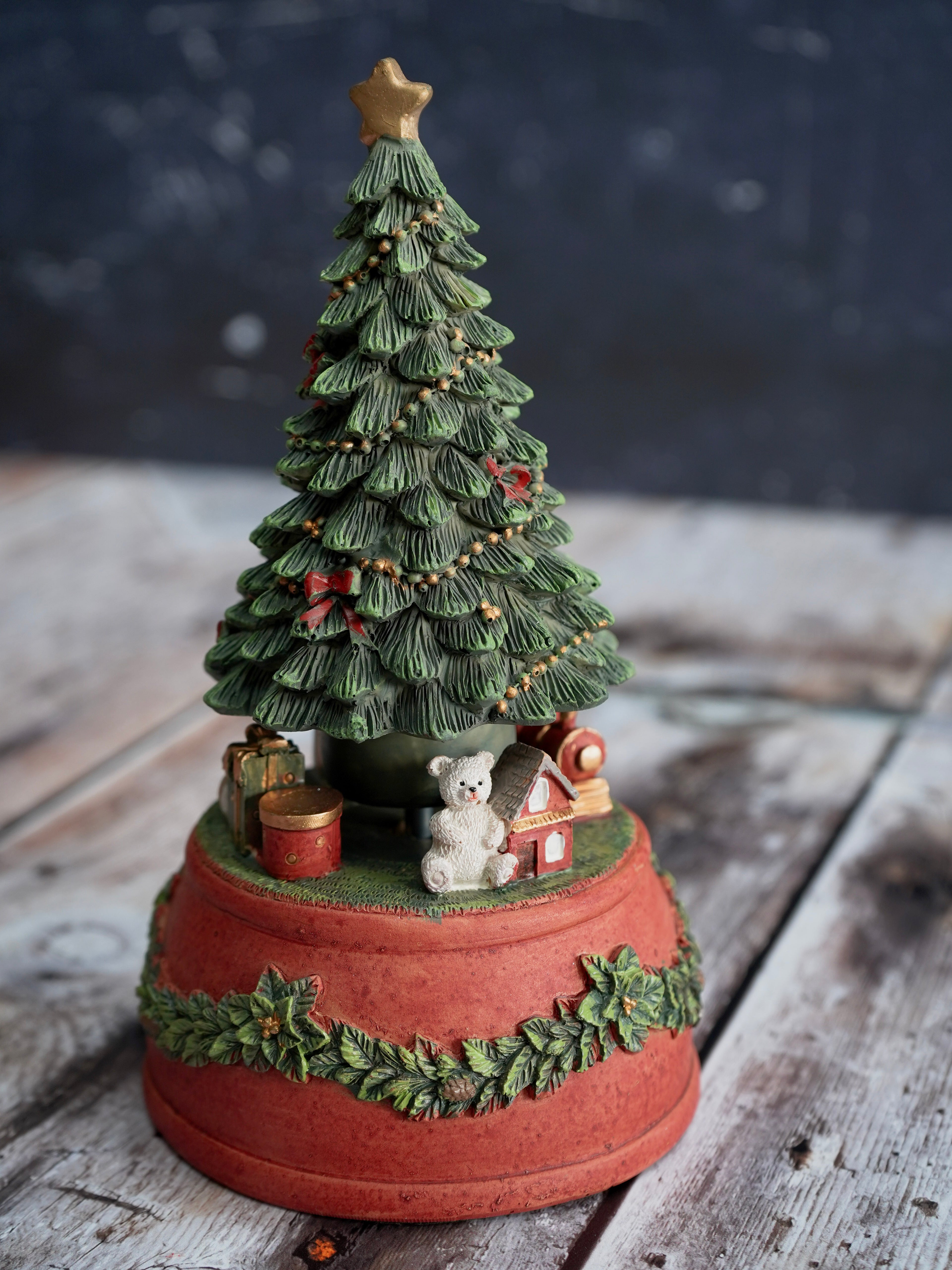 Decorative Christmas tree figurine with a star on top, surrounded by small toys and ornaments, on a rustic wooden surface.
