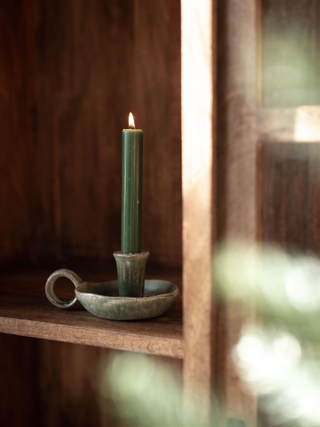 Green candle in a rustic ceramic holder on a wooden shelf