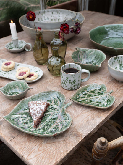 Ceramic tableware including bowls, plates, and mugs on a wooden table with a rustic setting.