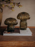 Two ribbed glass mushroom-shaped decorative tabletop lamps in a smoky amber-brown color, displayed on a stack of books on a woven mat.