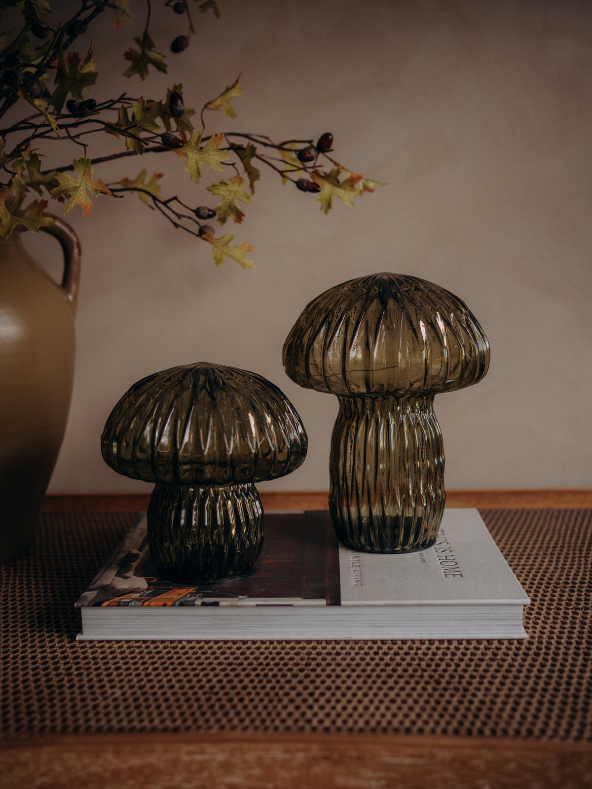 Two ribbed mushroom-shaped glass led table lamps in a smoky translucent brown color, displayed on a stack of books on a woven mat.