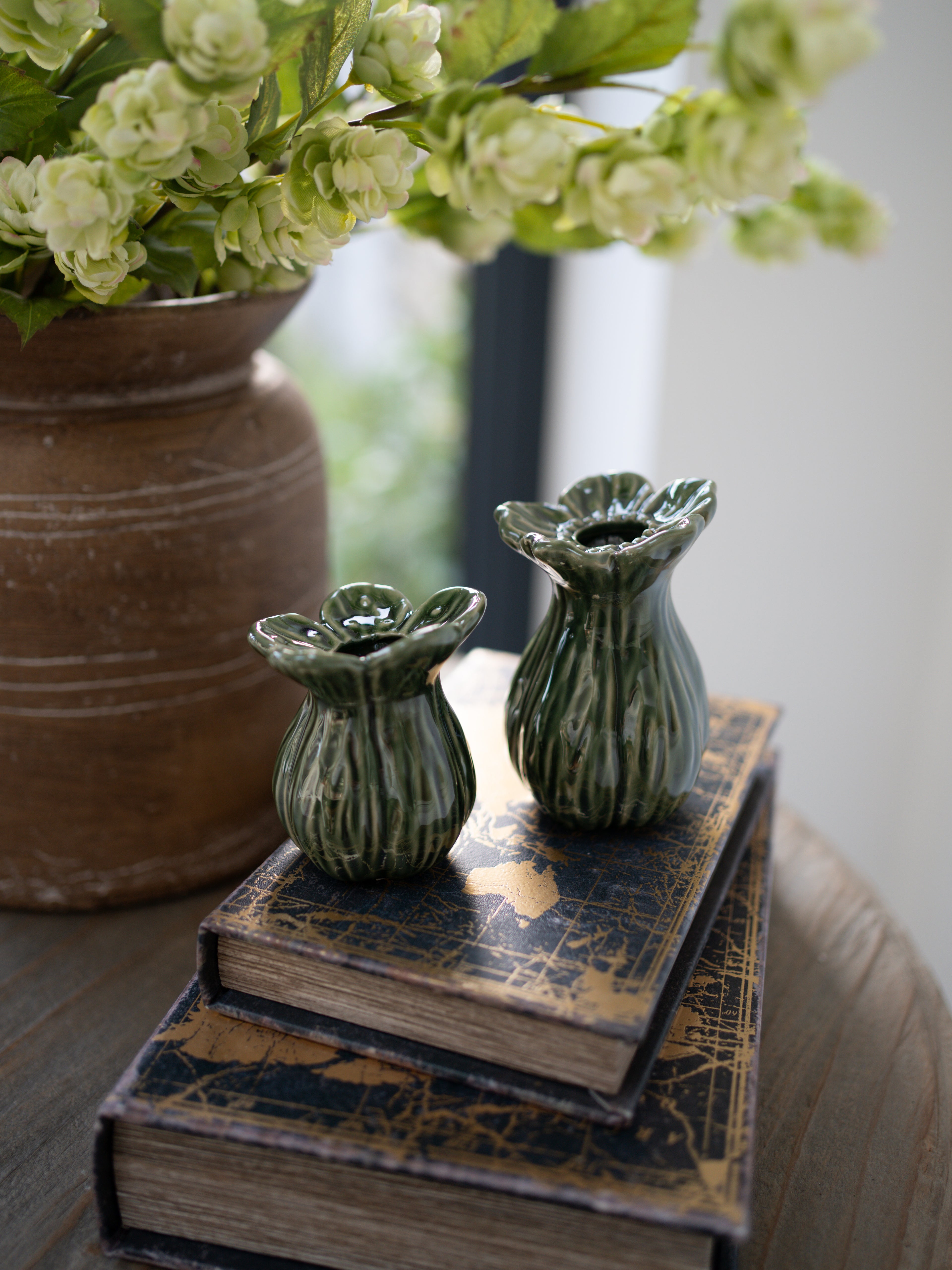 Two green ceramic vases on a stack of books with a blurred background