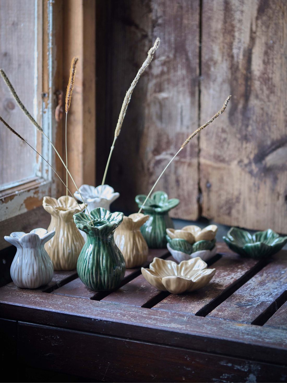 Collection of small ceramic bud vases and bowls on a wooden surface with a rustic background.
