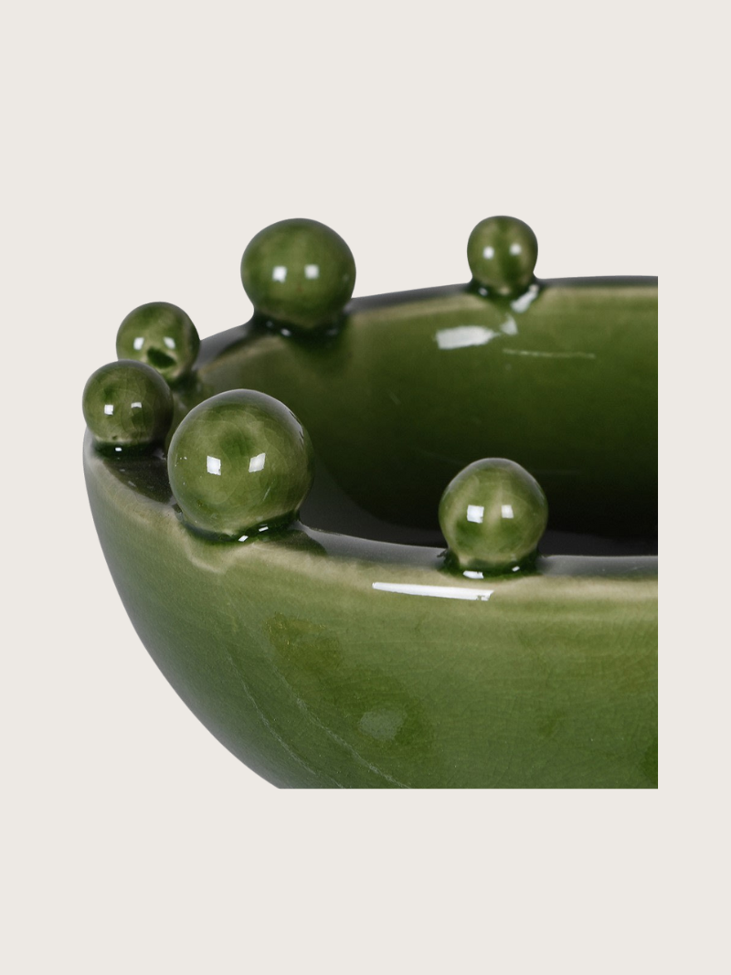 Green ceramic bowl with spherical decorations on a beige background