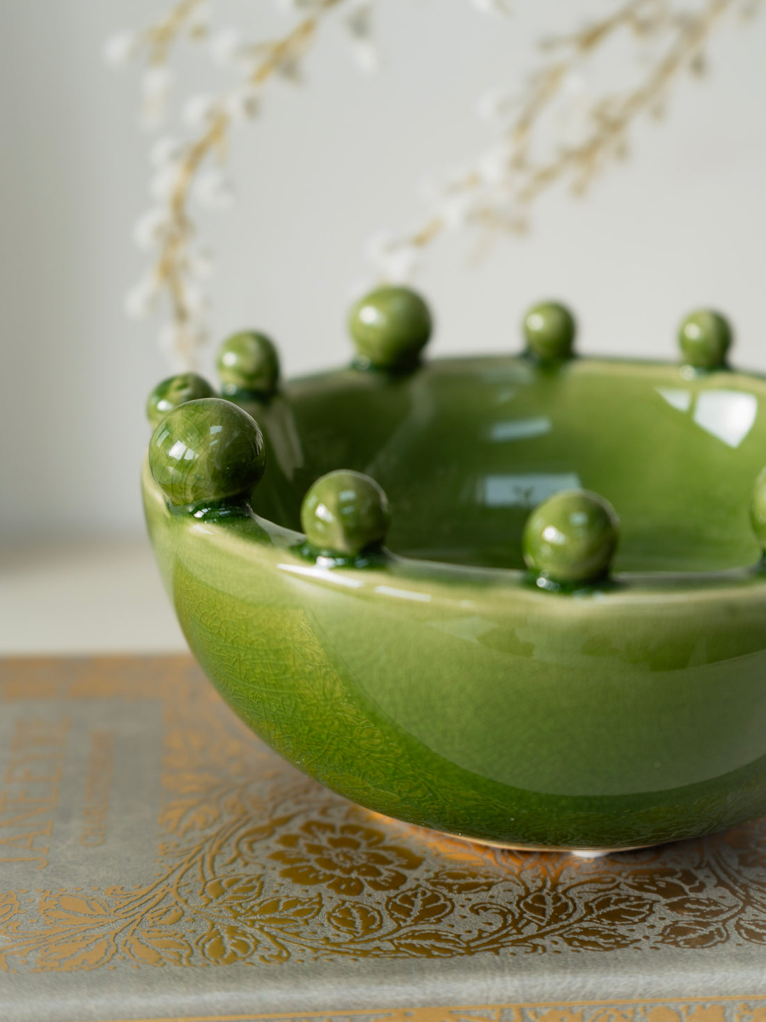 Green ceramic bowl with spherical bobble protrusions on a decorative surface