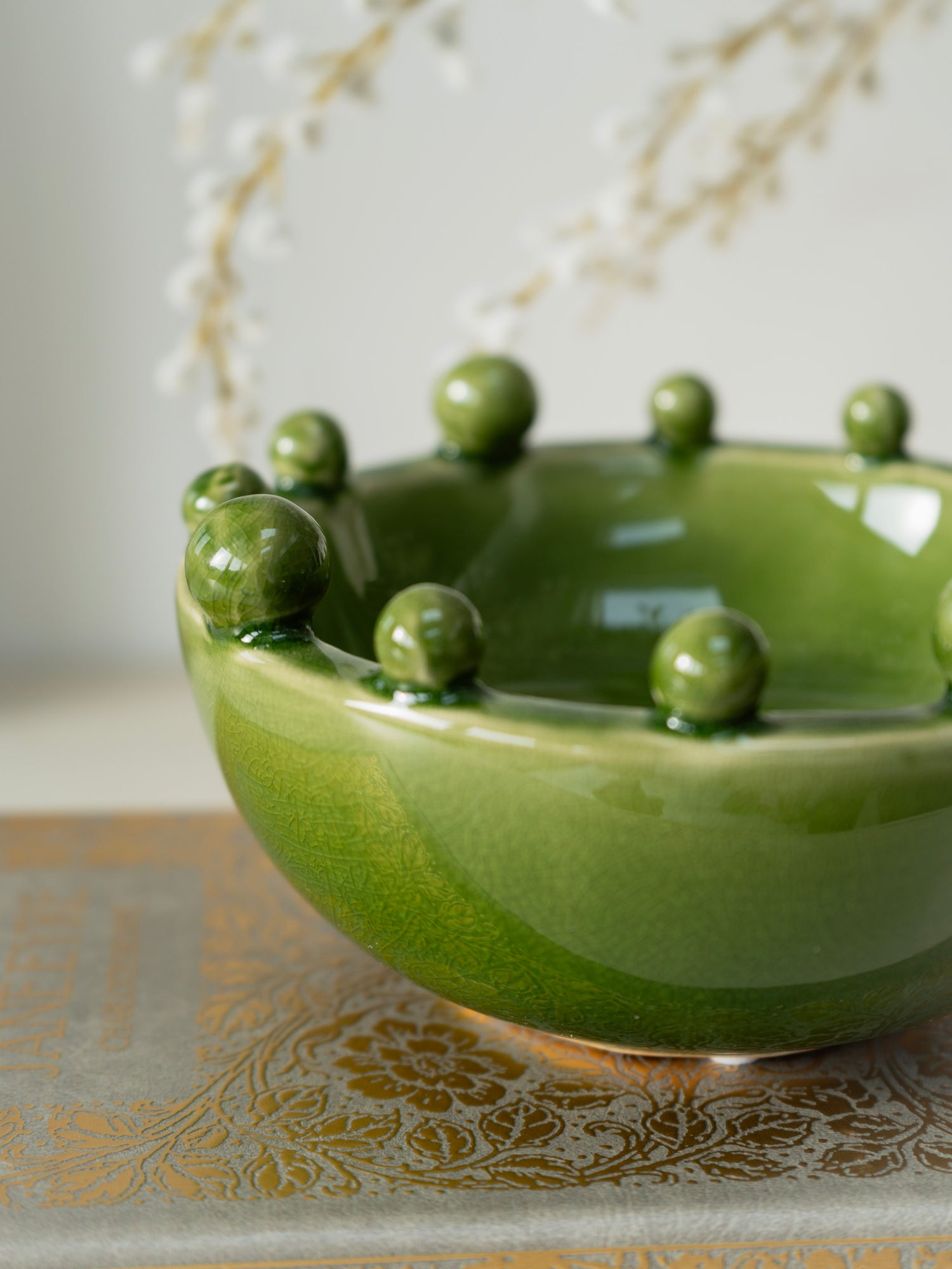 Green ceramic bowl with spherical bobble protrusions on a decorative surface