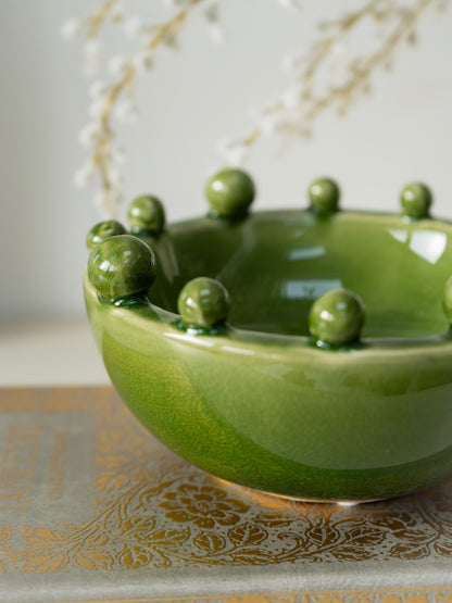 Green ceramic bowl with spherical bobble protrusions on a decorative surface