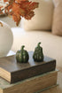 Two green decorative pumpkins on a book with autumn leaves in the background